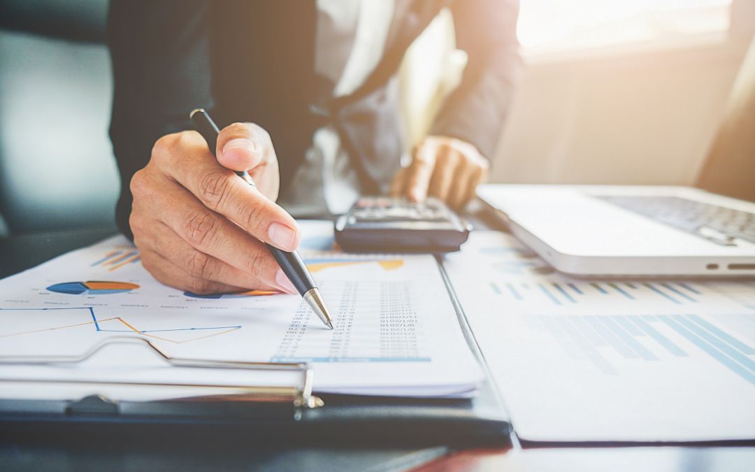 Persona revisando gráficos financieros y calculando cifras en un escritorio, representando la gestión financiera empresarial.