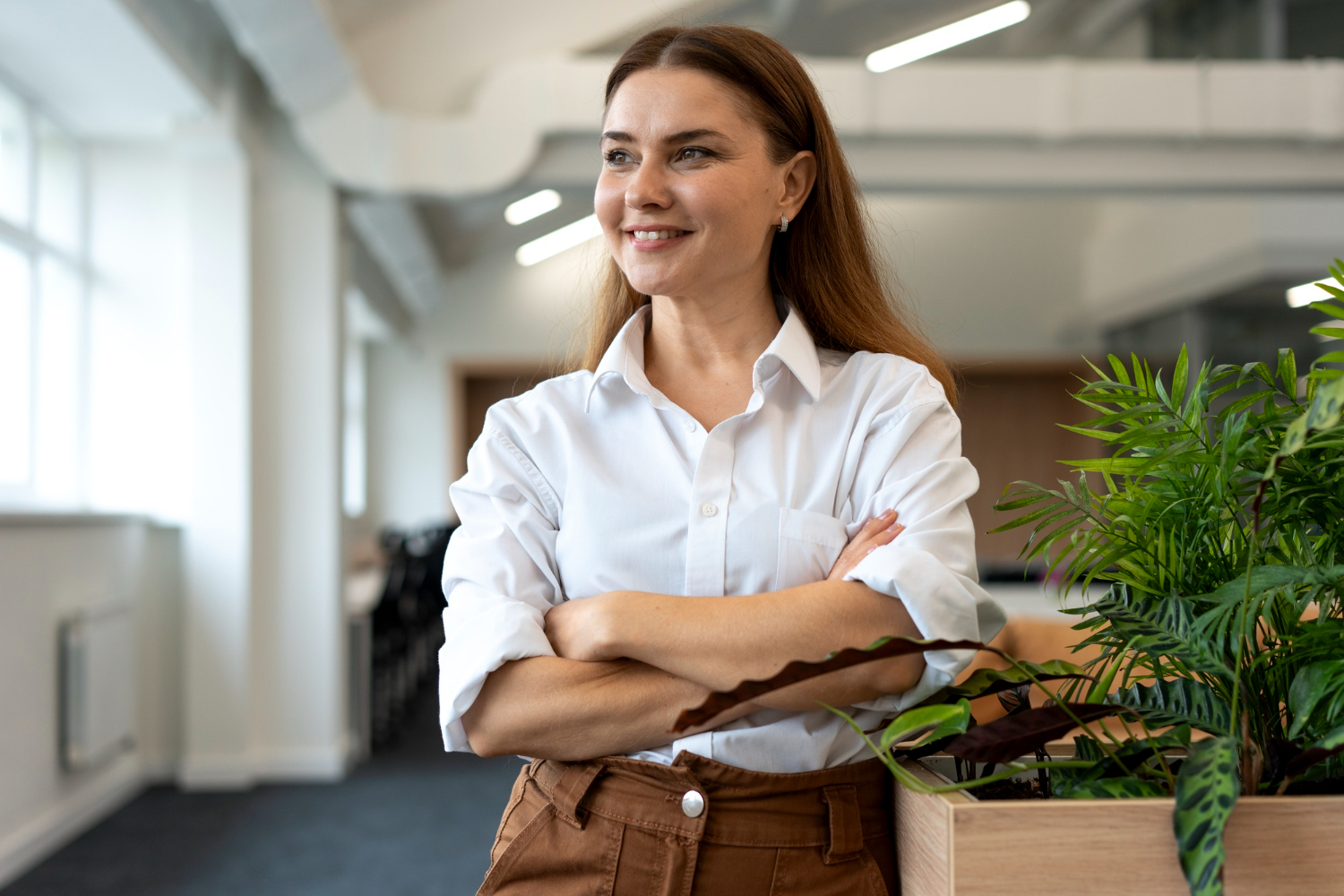 Mujer joven fundadora de un emprendimiento femenino, mira a través de una ventana, con gesto de satisfacción.
