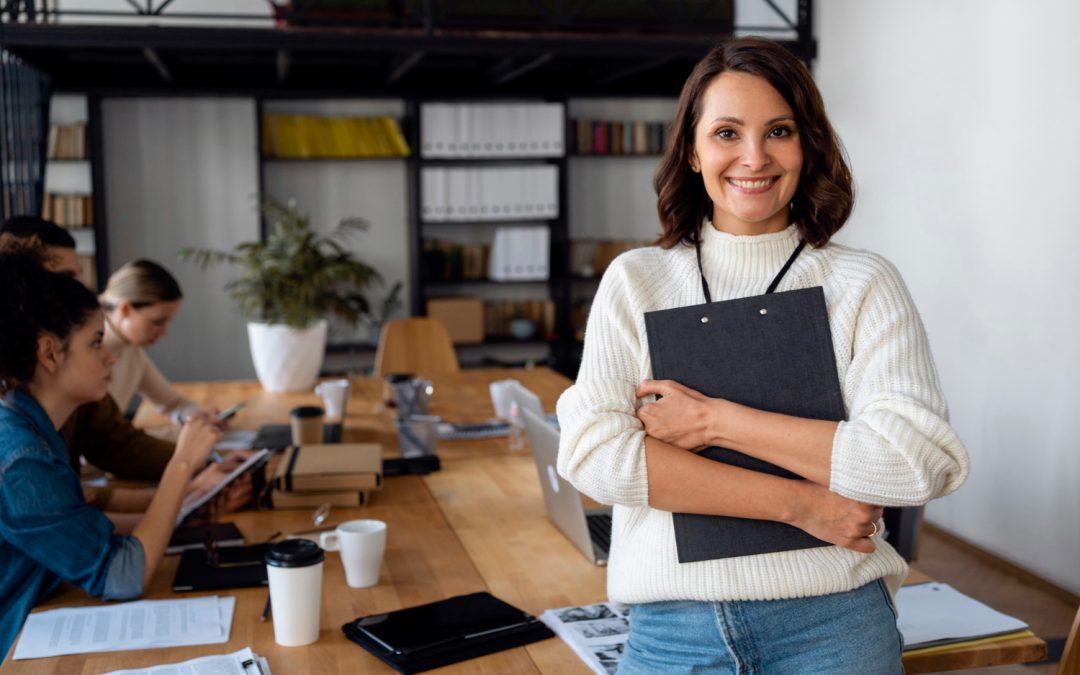 Mujer emprendedora sonríe satisfecha, de fondo se observa una sala de juntas con personas que trabajan en su empresa.
