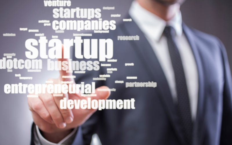 Empresario señala la palabra “startup” en una nube de conceptos clave, ilustrando ejemplos de empresas emergentes exitosas.