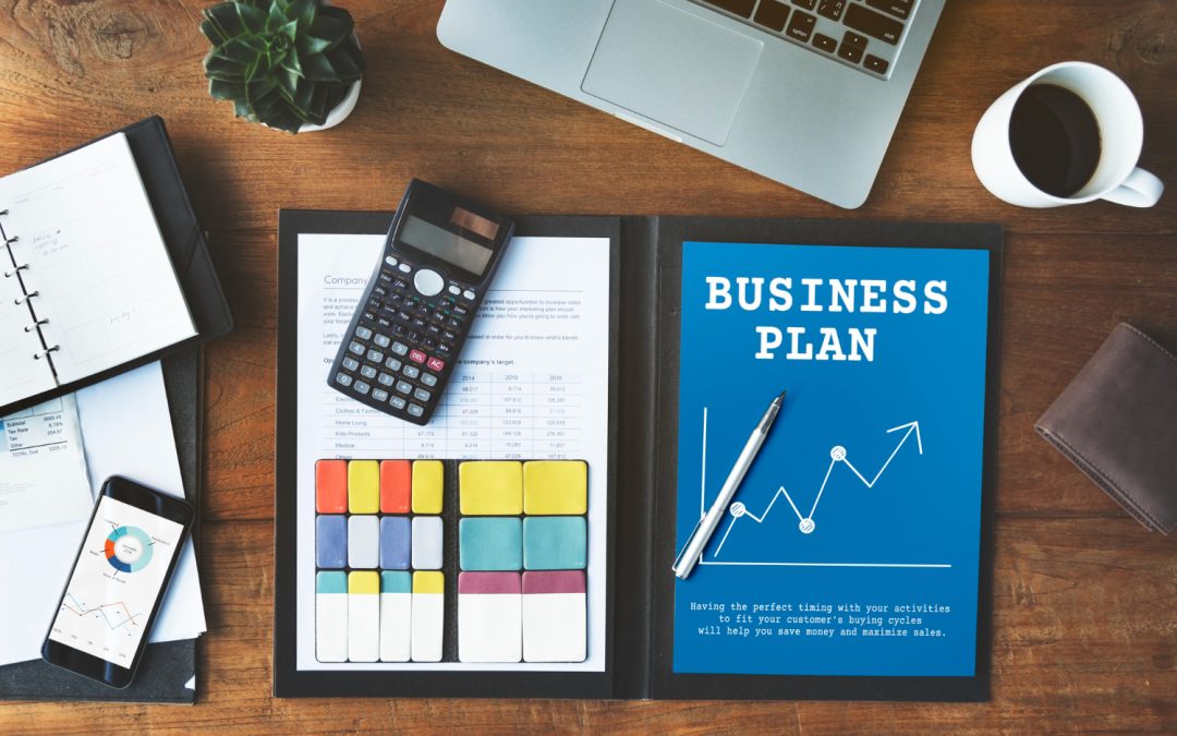Un escritorio de madera con una laptop, taza de café, calculadora, un cuaderno abierto mostrando un título de "BUSINESS PLAN" con un gráfico y un smartphone.