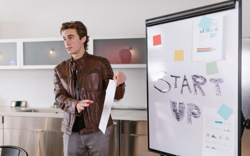Emprendedor joven explicando qué es una startup con gráficos en un rotafolio durante una reunión de trabajo.
