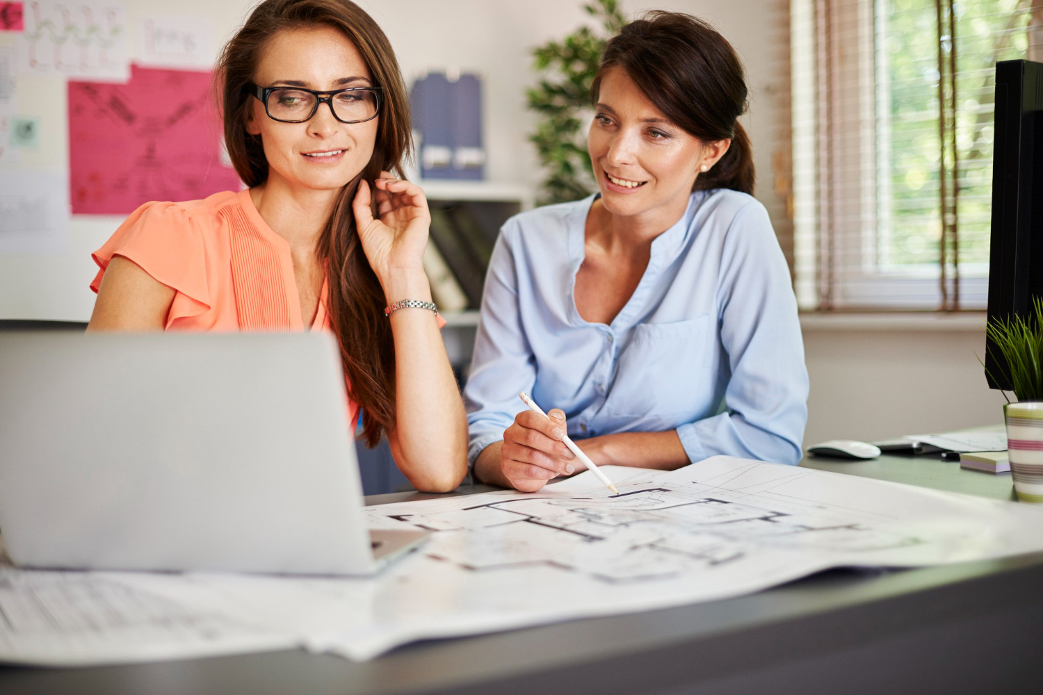 Dos mujeres, sentadas en un escritorio, ven la pantalla de una computadora para ilustrar las opciones de préstamo que existen en los bancos.
