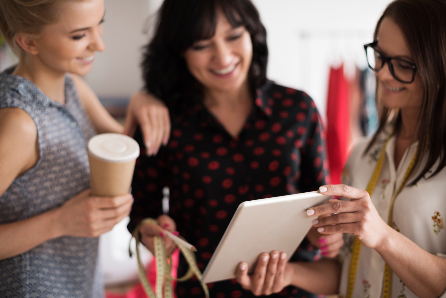 Tres mujeres miran una tableta y sonríen. La imagen ilustra una reunión de emprendedoras que forman parte de la industria de la moda. 