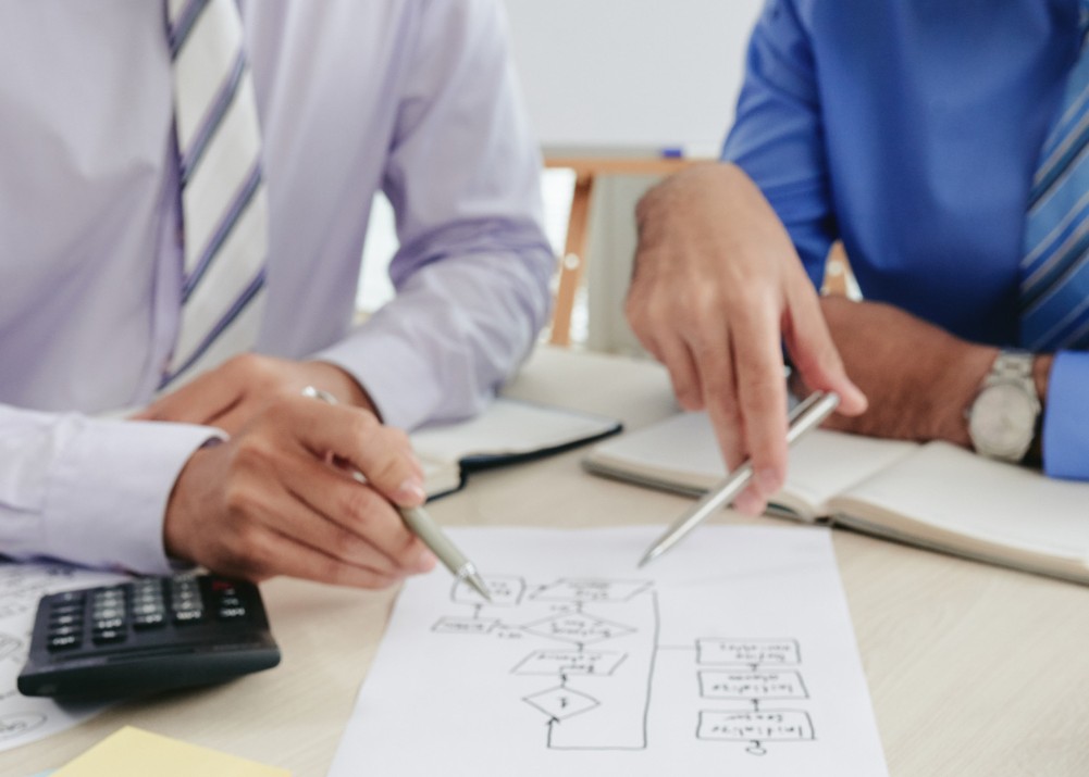 Vista de las manos de dos hombres que revisan un diagrama dibujado en un papel. La imagen ilustra las alternativas al plan de negocios tradicional.